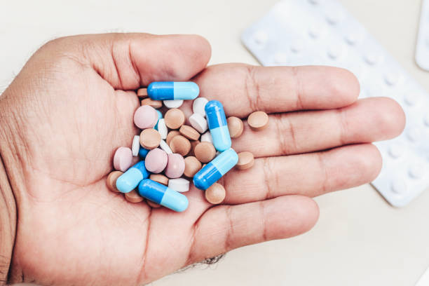 Hand of a man holding several medicine tablets.